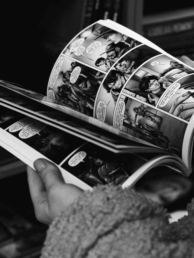 Reader holding open a single comic issue under warm lamp light